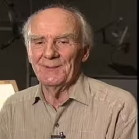Douglas Seale putting on a shirt with looks like a mix of brown and grey